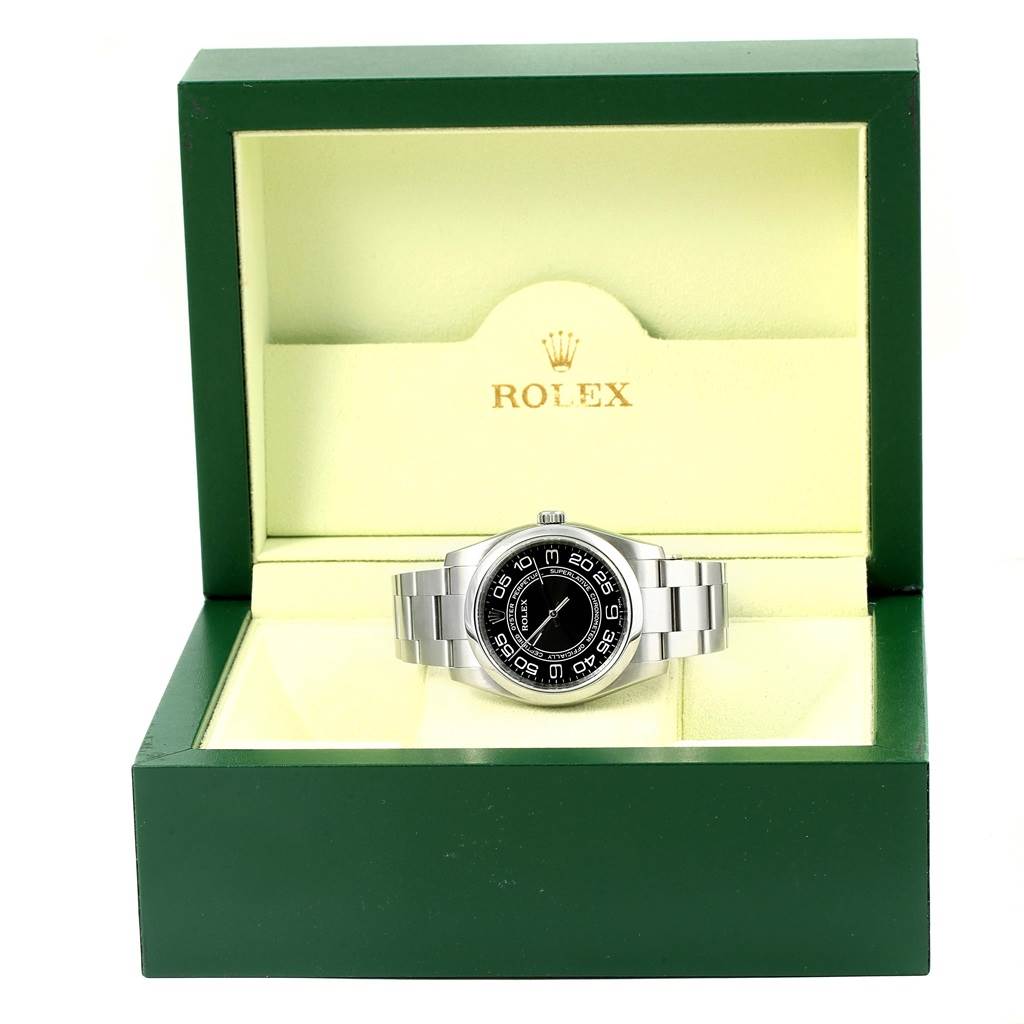 The Rolex Oyster Perpetual 116000 Men's Stainless Steel Black Dial 116000 Men's Stainless Steel Black Dial watch is shown from the front angle inside its green and beige branded box.