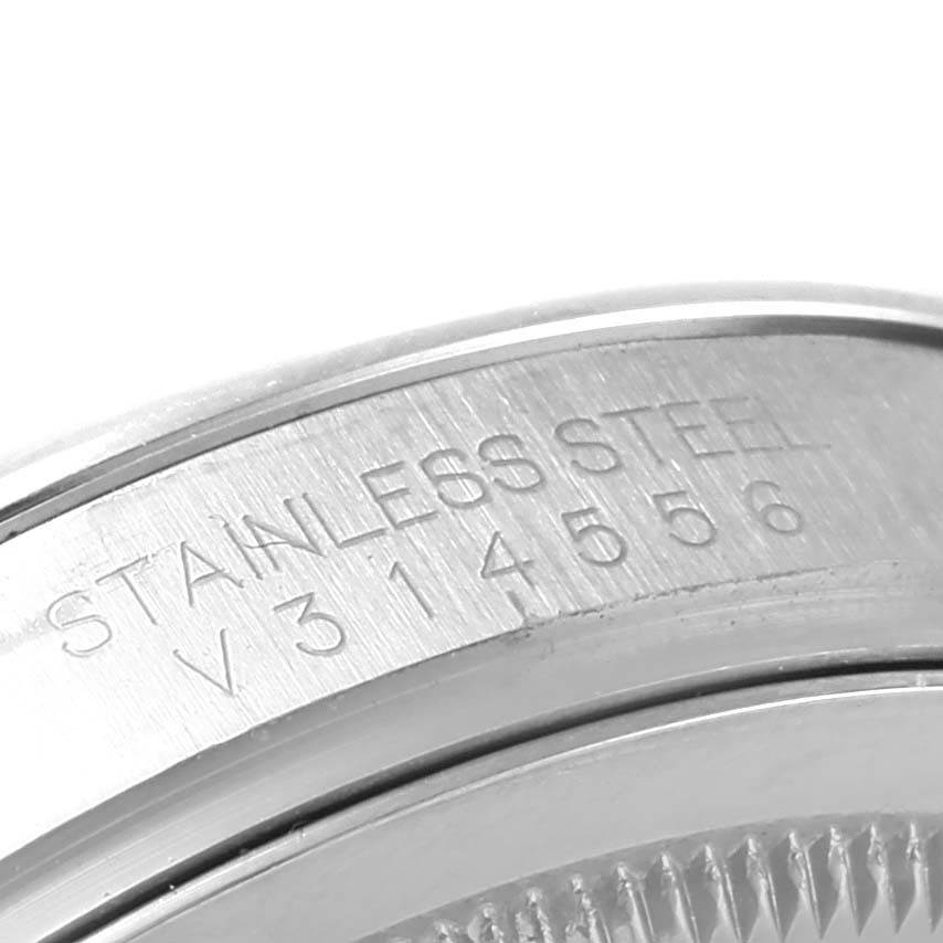 The image shows a close-up of the stainless steel casing with etched text on a Rolex Oyster Perpetual 116000 Men's Stainless Steel Silver Dial 116000 Men's Stainless Steel Silver Dial watch.