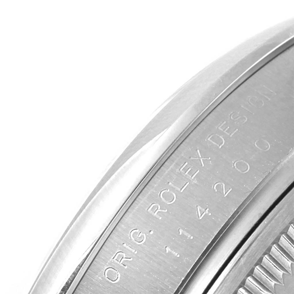The image shows a close-up view of the side of a Rolex Oyster Perpetual 114200 Stainless Steel Champagne Dial 114200 Stainless Steel Champagne Dial watch case, displaying the engraving and serial number.