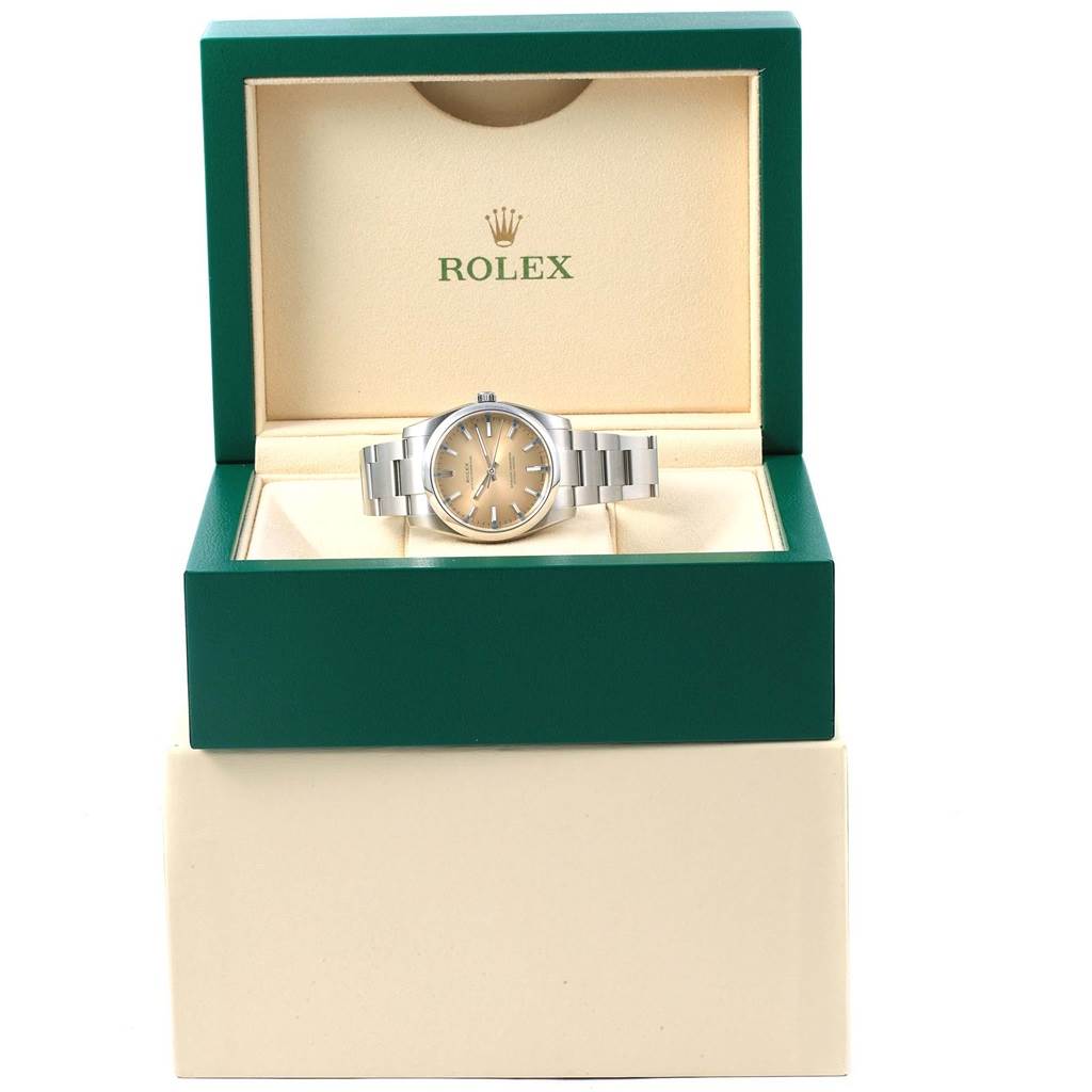 The Rolex Oyster Perpetual 114200 Stainless Steel Champagne Dial 114200 Stainless Steel Champagne Dial watch is shown front-facing inside its green and beige presentation box.