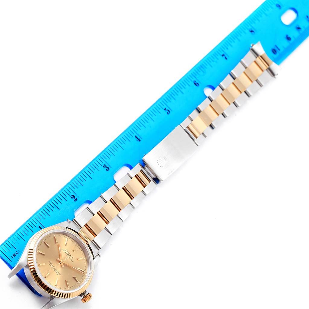 The image shows a Rolex Oyster Perpetual 14233 Men's Steel and Gold (two tone) Champagne Dial 14233 Men's Steel and Gold (two tone) Champagne Dial watch lying flat alongside a blue ruler, displaying its face and two-tone bracelet.