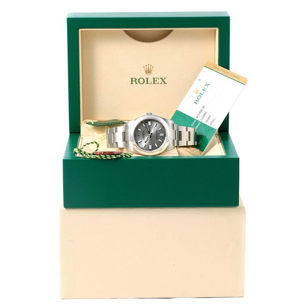 The image shows a Rolex Oyster Perpetual 116000 Men's Stainless Steel Grey Dial 116000 Men's Stainless Steel Grey Dial watch from a front angle in its open box, accompanied by warranty cards and tags.
