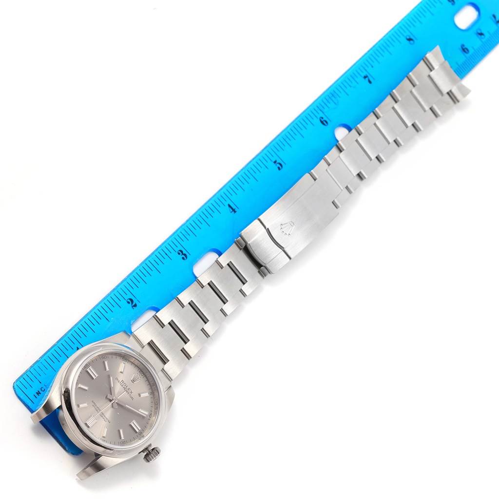 The image shows a Rolex Oyster Perpetual 116000 Stainless Steel Grey Dial 116000 Stainless Steel Grey Dial watch laid flat with the face visible, next to a blue ruler for scale.