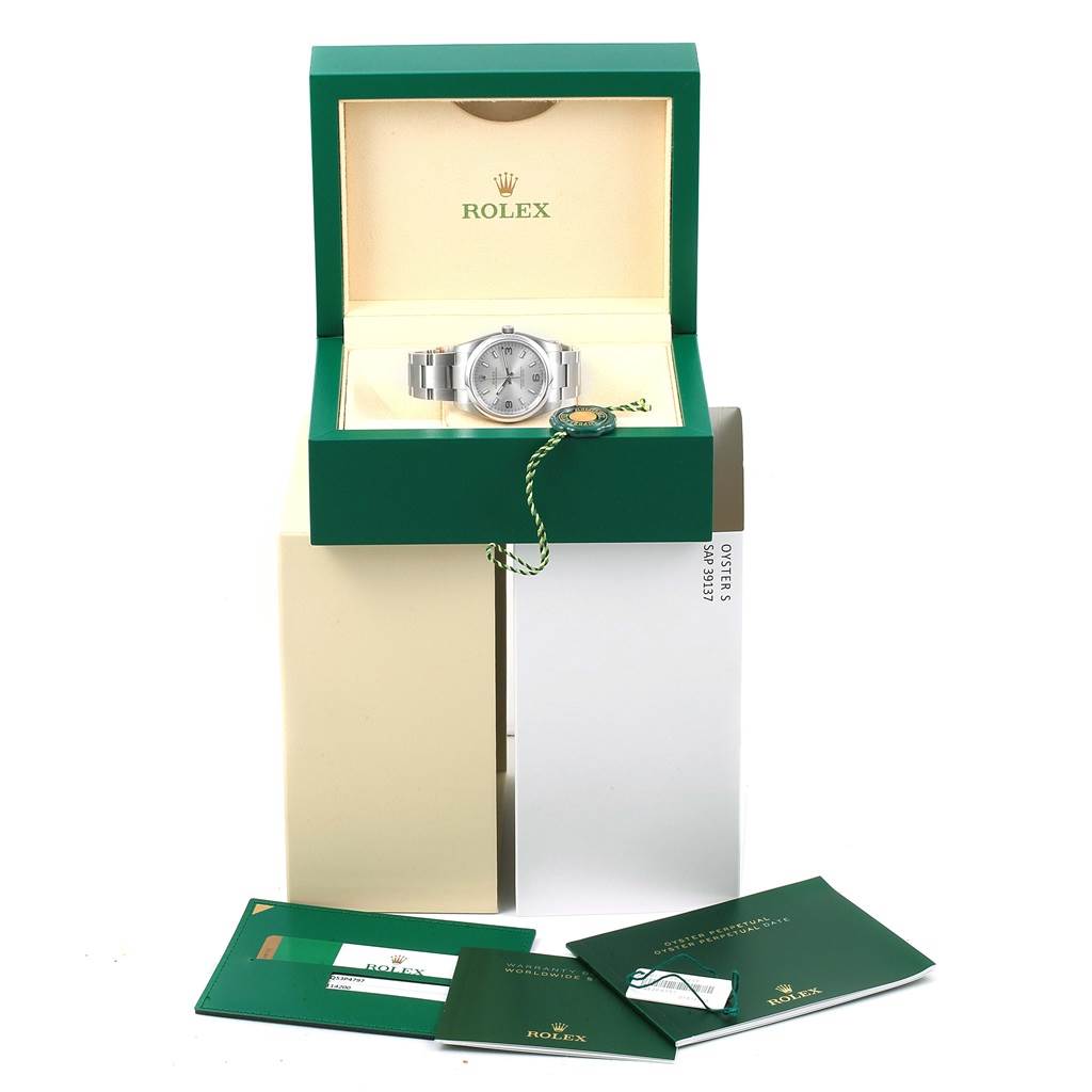 The image shows a Rolex Oyster Perpetual 114200 Men's Stainless Steel Silver Dial 114200 Men's Stainless Steel Silver Dial watch in its open green box, with accompanying booklets and accessories.