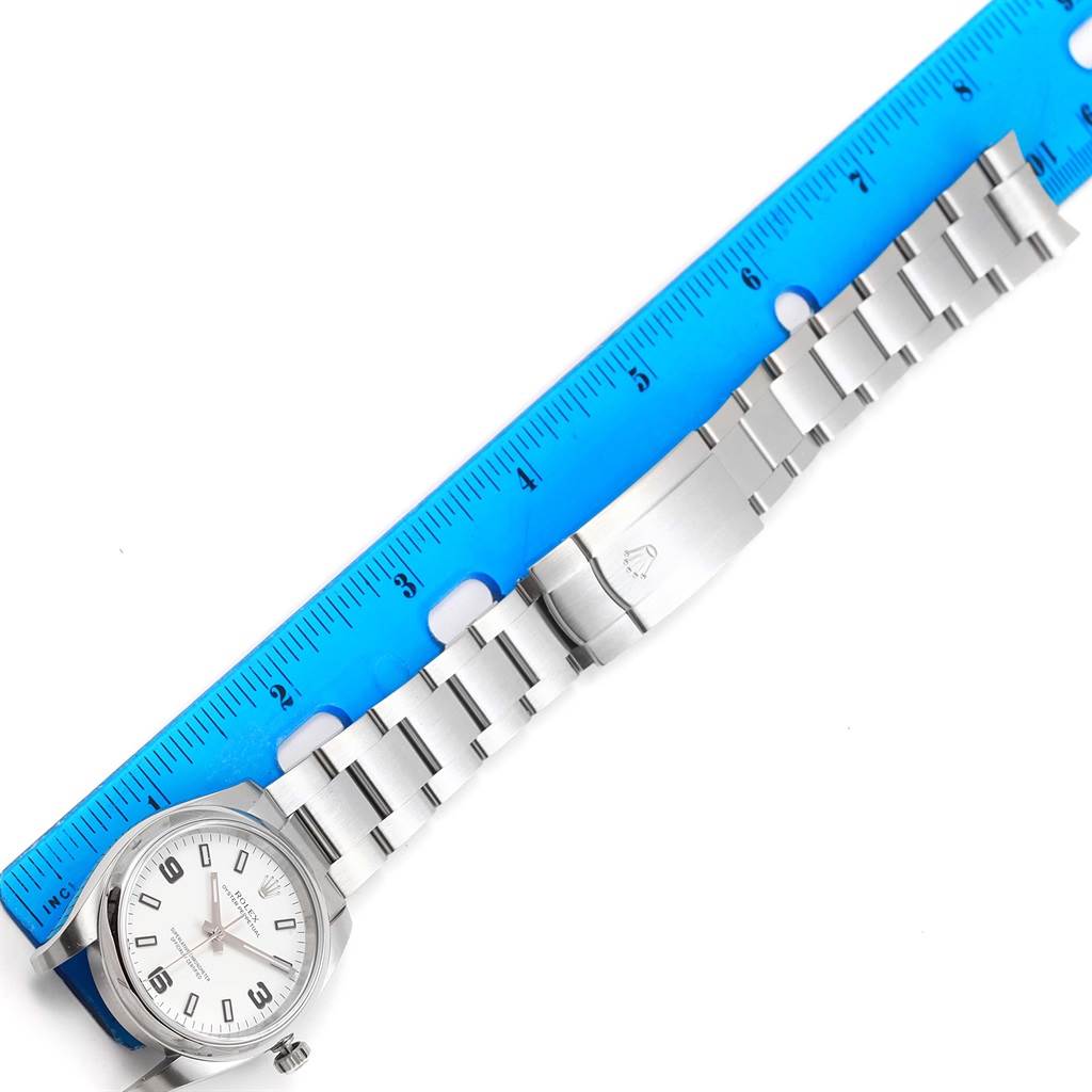 The image shows a top-down view of the Rolex Oyster Perpetual 114200 Stainless Steel White Dial 114200 Stainless Steel White Dial watch along with a blue ruler measuring its length.