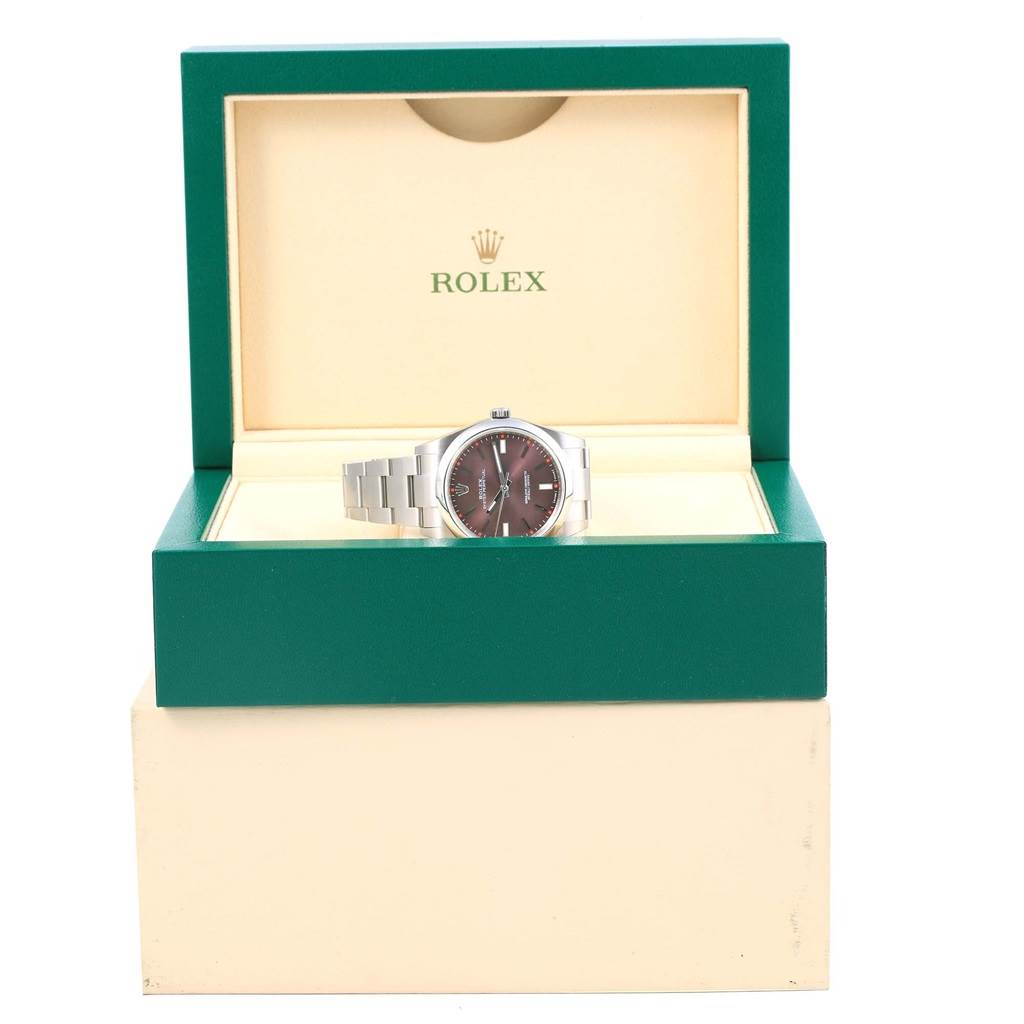 The image shows a Rolex Oyster Perpetual 114300 Stainless Steel Burgundy Dial 114300 Stainless Steel Burgundy Dial watch placed inside an open green and cream-colored Rolex box.
