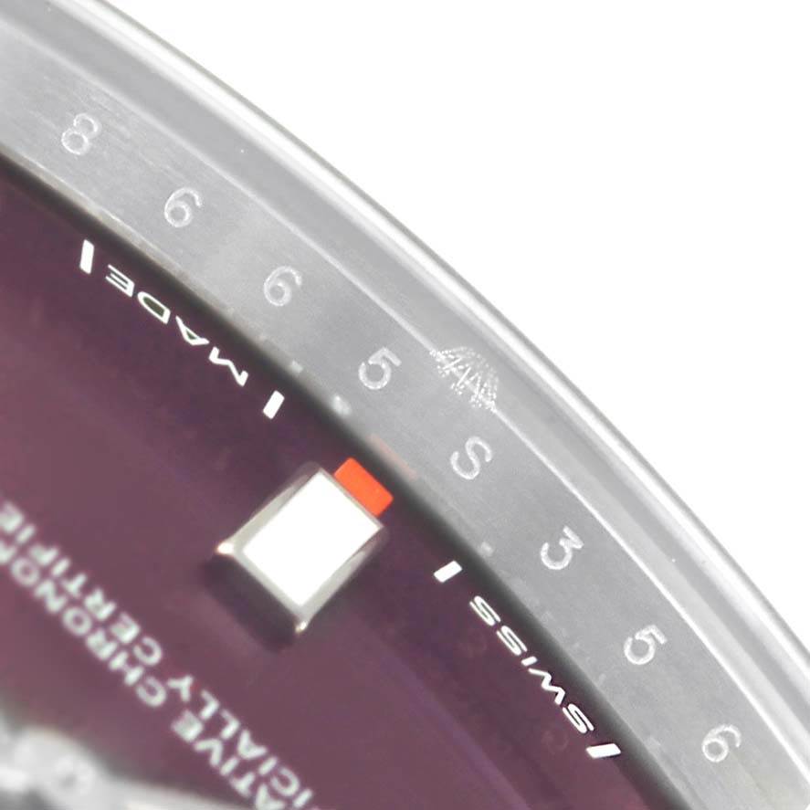 The image shows a close-up of the dial and bezel of a Rolex Oyster Perpetual 114300 Stainless Steel Burgundy Dial 114300 Stainless Steel Burgundy Dial watch, focusing on the numerical markers and text details.