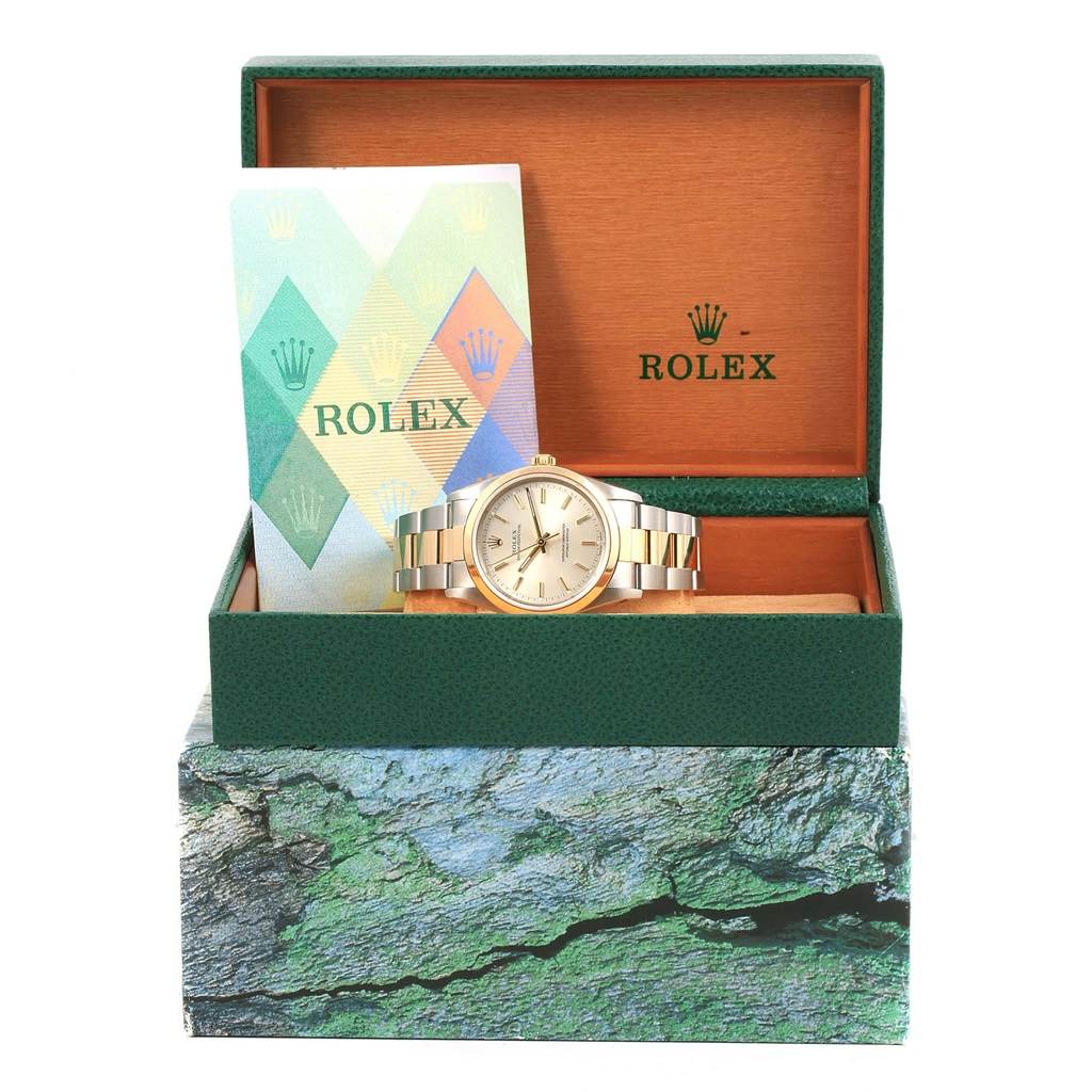 This image shows a Rolex Oyster Perpetual 14203 Steel and Gold (two tone) Silver Dial 14203 Steel and Gold (two tone) Silver Dial watch from a front angle in an open green and orange box with a certificate booklet.