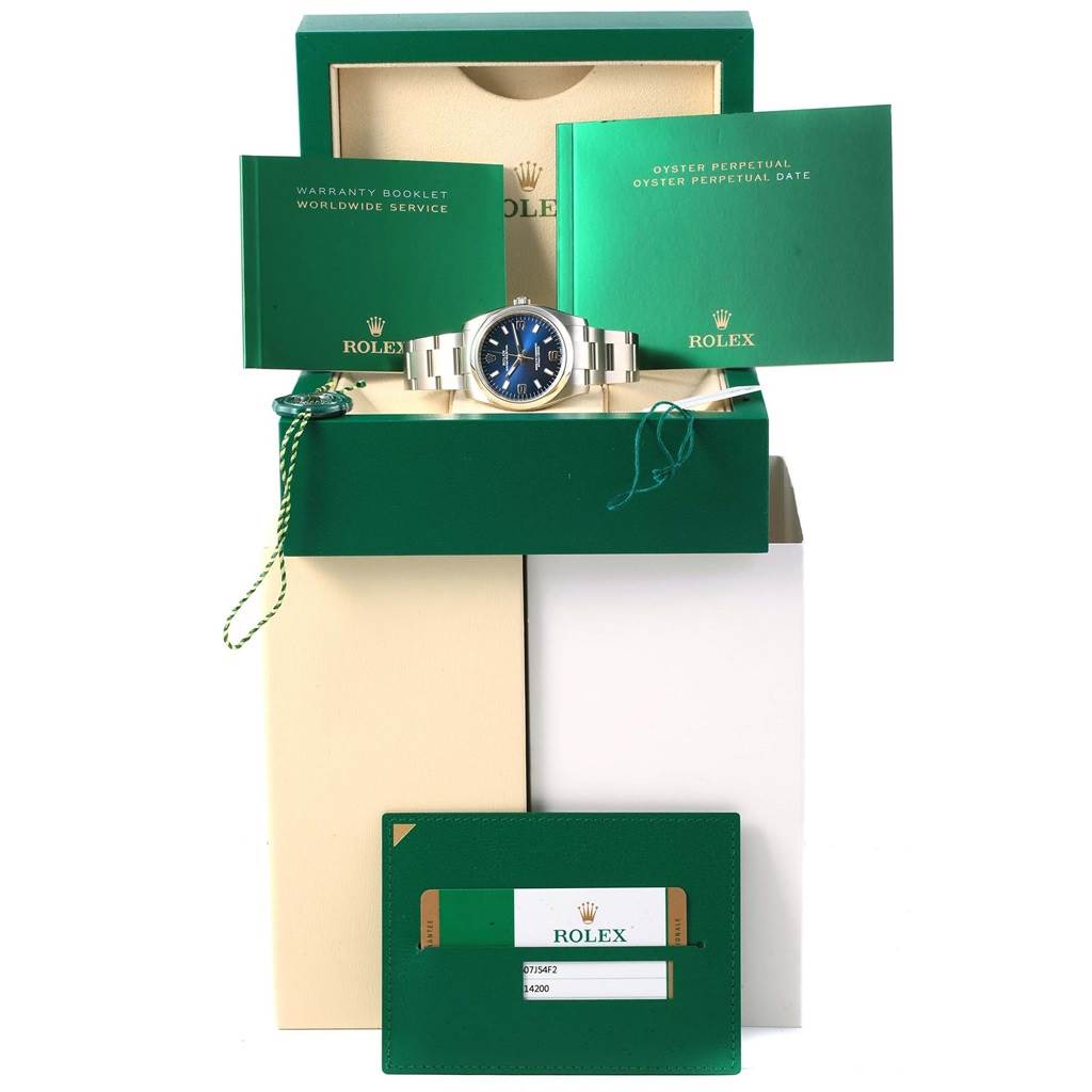 The image shows a front view of a Rolex Oyster Perpetual 114200 Men's Stainless Steel Blue Dial 114200 Men's Stainless Steel Blue Dial watch, warranty booklet, instruction manual, and certification card.