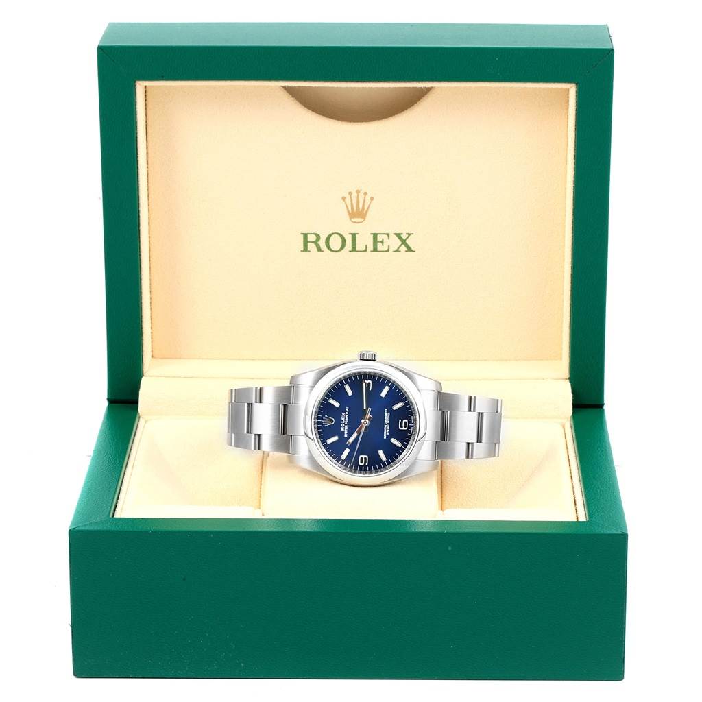 This photo shows a Rolex Oyster Perpetual 116000 Men's Stainless Steel Blue Dial 116000 Men's Stainless Steel Blue Dial watch displayed frontally in an open green and beige box.