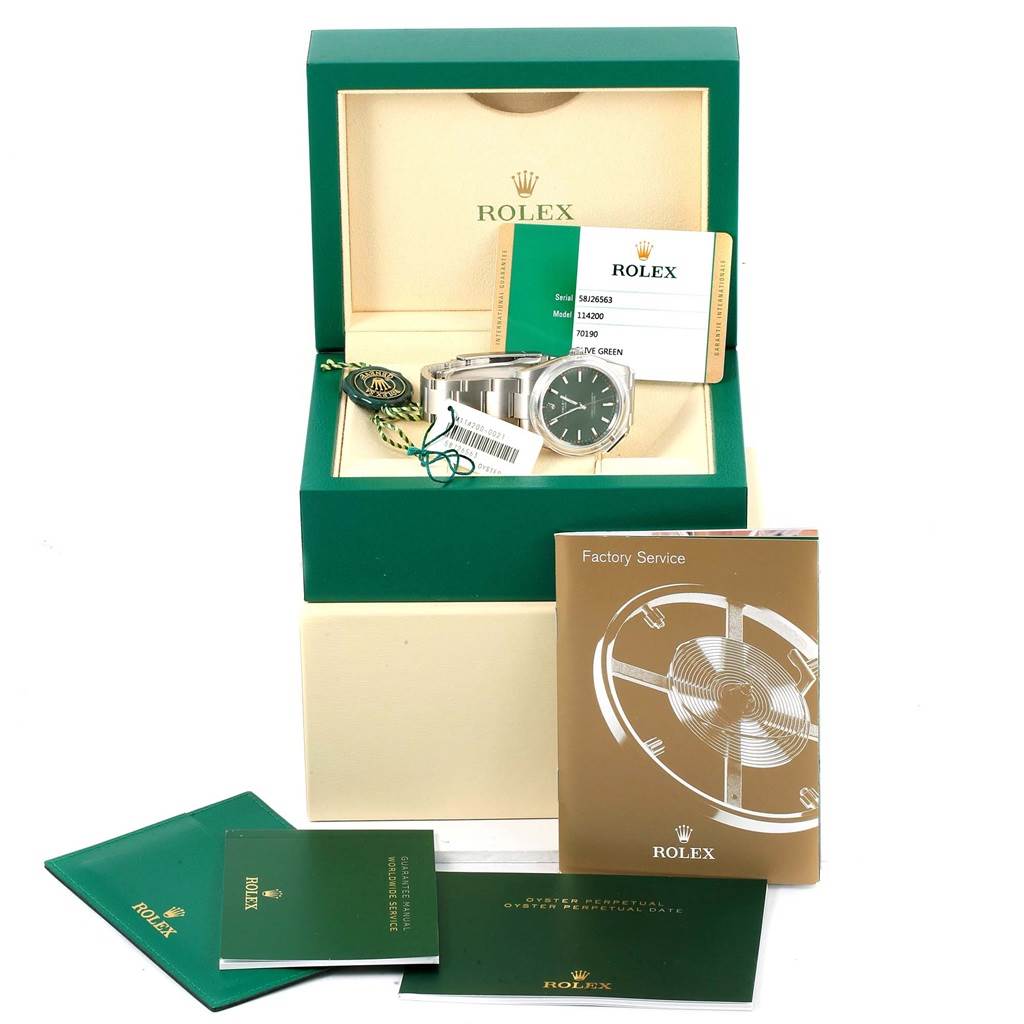The image shows a Rolex Oyster Perpetual 114200 Stainless Steel Green Dial 114200 Stainless Steel Green Dial watch with its box, tags, warranty card, and booklets from a front angle.