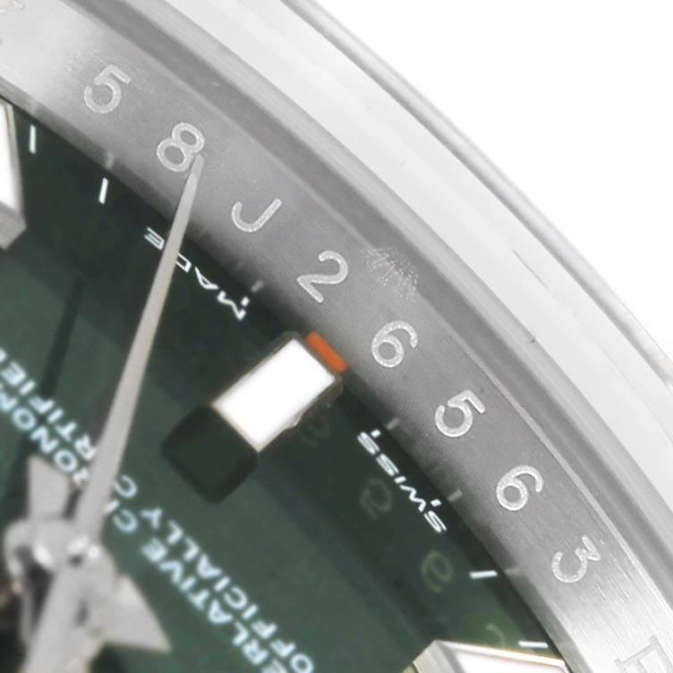 The image shows a partial view of a Rolex Oyster Perpetual 114200 Stainless Steel Green Dial 114200 Stainless Steel Green Dial watch, focusing on the dial, hour markers, and part of the bezel.