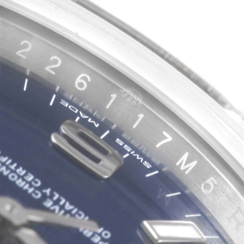 The image shows a close-up of the bezel and part of the dial of a Rolex Oyster Perpetual 114200 Men's Stainless Steel Blue Dial 114200 Men's Stainless Steel Blue Dial watch, highlighting some numbers and markers.