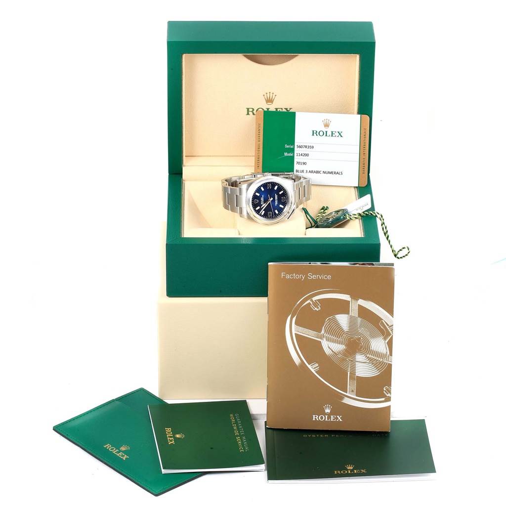 The image shows a Rolex Oyster Perpetual 114200 Men's Stainless Steel Blue Dial 114200 Men's Stainless Steel Blue Dial watch in its box with documents and accessories displayed.