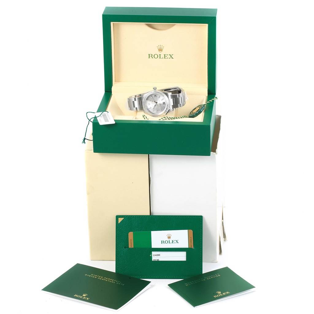 The Rolex Oyster Perpetual 114200 Stainless Steel Silver Dial 114200 Stainless Steel Silver Dial watch is displayed in an open green box with accompanying documents and tags.