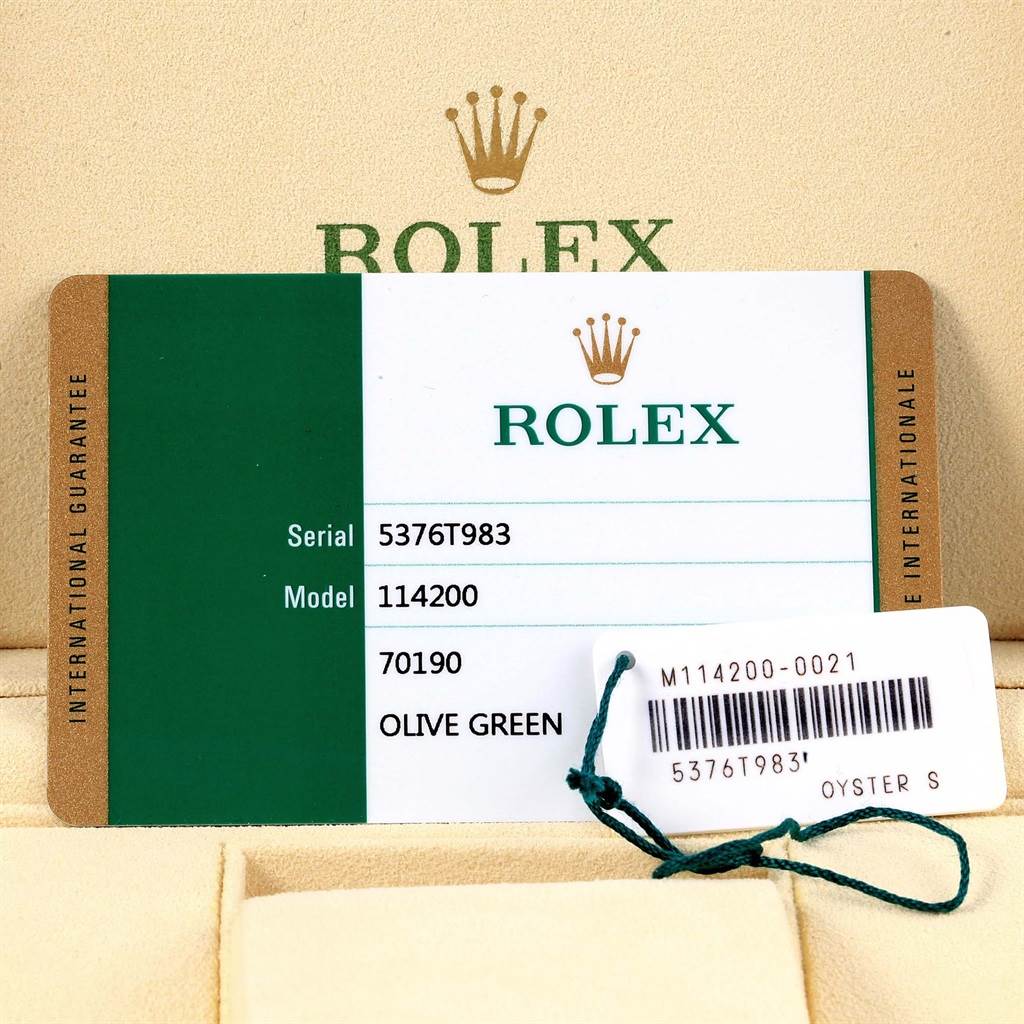 The image shows the warranty card and tags of a Rolex Oyster Perpetual 114200 Stainless Steel Green Dial 114200 Stainless Steel Green Dial model 114200, with a green and white design.