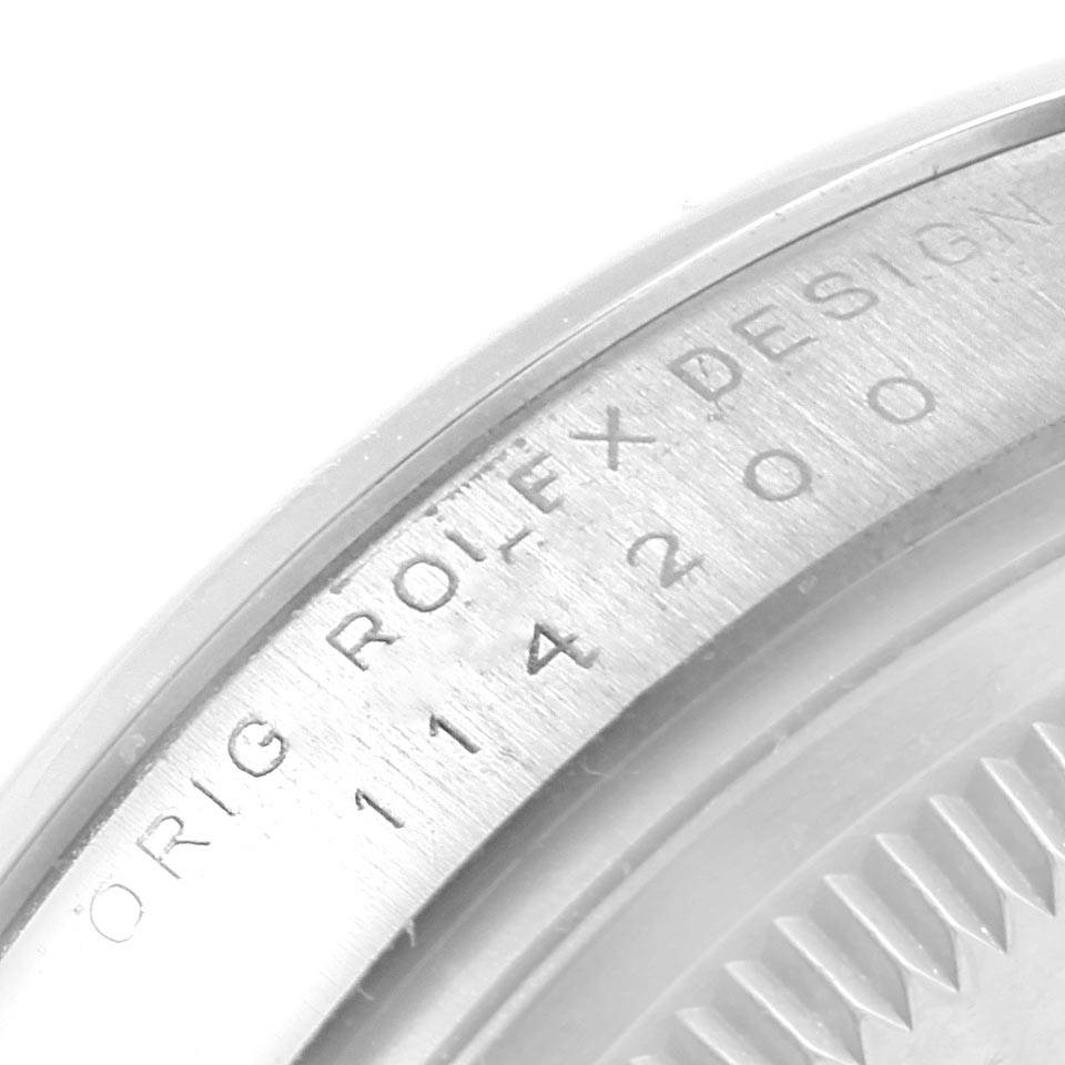 The image shows a close-up of the engraved outer rim and case back of a Rolex Oyster Perpetual 114200 Stainless Steel Burgundy Dial 114200 Stainless Steel Burgundy Dial watch.