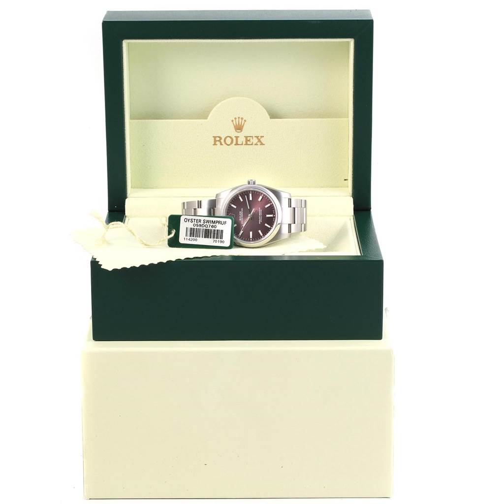 The image shows a Rolex Oyster Perpetual 114200 Stainless Steel Burgundy Dial 114200 Stainless Steel Burgundy Dial watch in an open green and beige Rolex box, shot from the front angle.