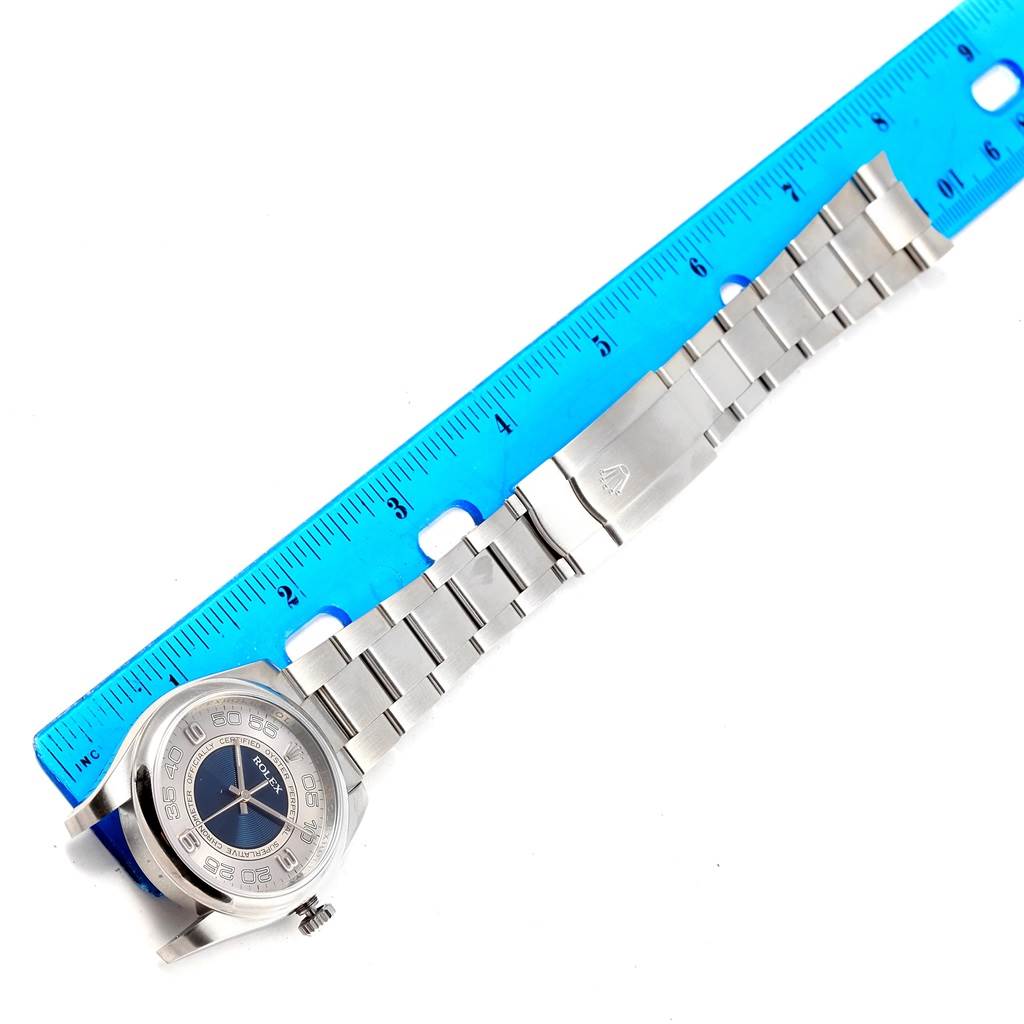 The Rolex Oyster Perpetual 116000 Men
s Stainless Steel Silver Dial 116000 Men
s Stainless Steel Silver Dial watch is shown from a top-down angle, with the full band and part of a ruler visible.