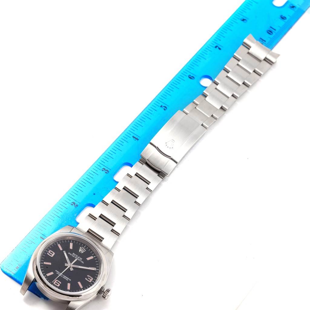 The image shows a Rolex Oyster Perpetual 116000 Men's Stainless Steel Black Dial 116000 Men's Stainless Steel Black Dial watch laid flat with a ruler beside it, displaying the dial, bracelet, and clasp.