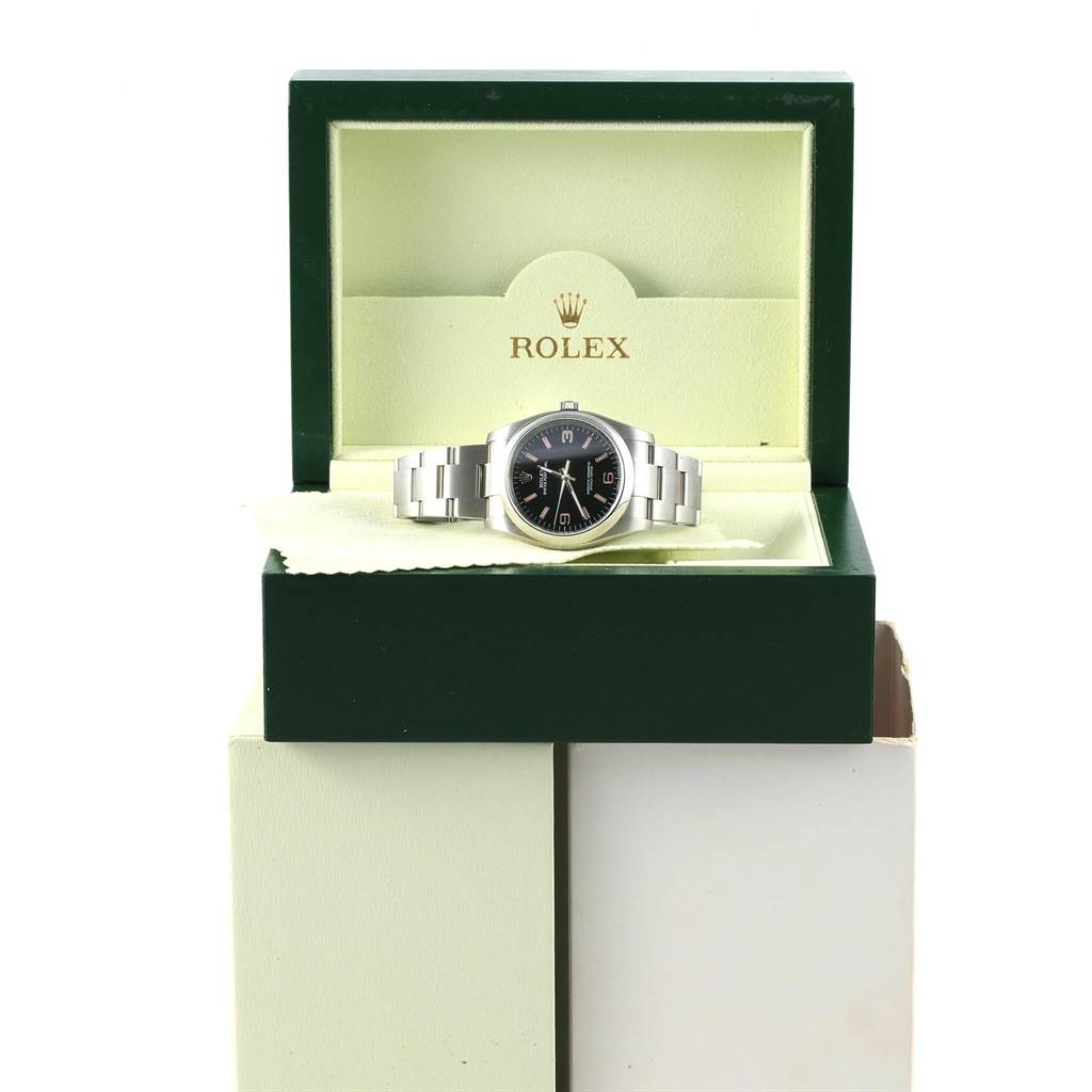 The Rolex Oyster Perpetual 116000 Men's Stainless Steel Black Dial 116000 Men's Stainless Steel Black Dial watch is displayed in its green box, showing the watch face and bracelet from a frontal angle.