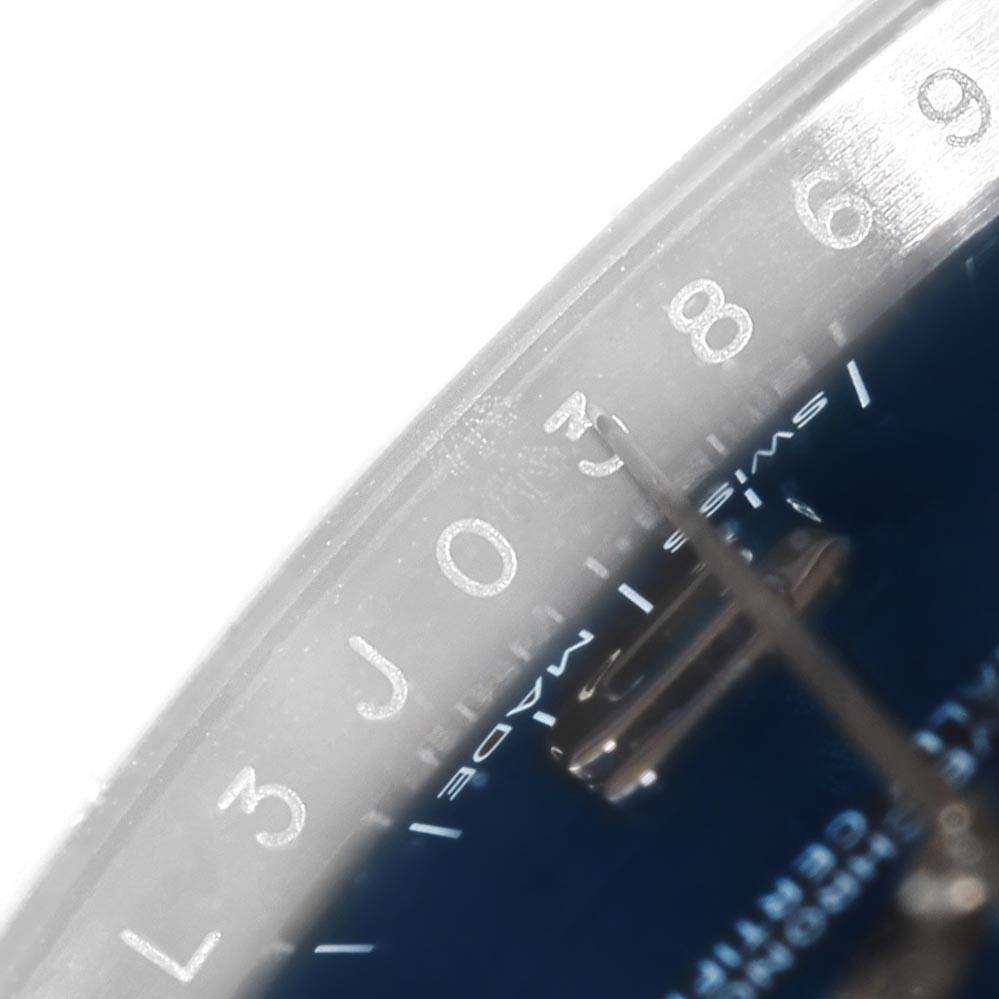 This close-up image shows part of the dial and the minute hand of a Rolex Oyster Perpetual 114200 Men's Stainless Steel Blue Dial 114200 Men's Stainless Steel Blue Dial watch, focused on the numerals and text.