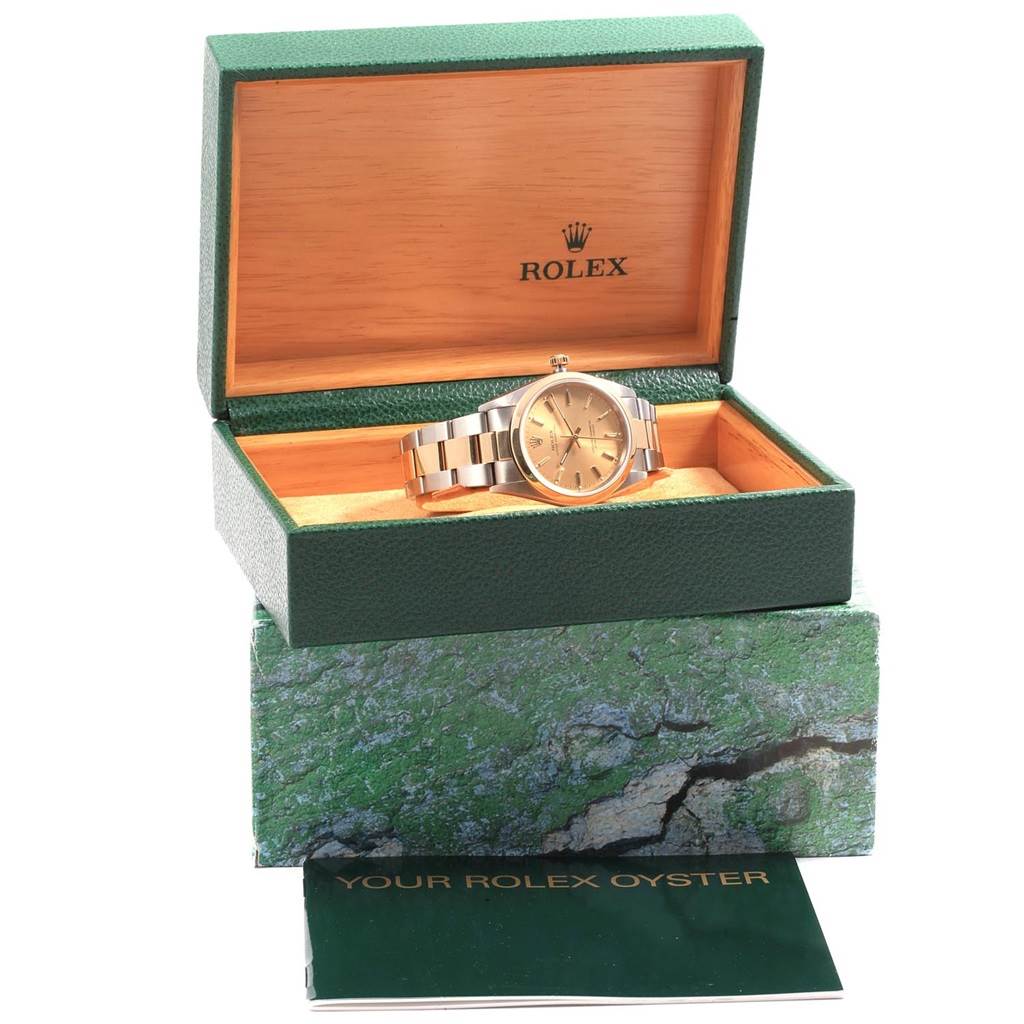 The Rolex Oyster Perpetual 14203 Men
s Steel and Gold (two tone) Champagne Dial 14203 Men
s Steel and Gold (two tone) Champagne Dial watch is displayed at an angle inside an open green and wooden box, with accompanying booklet and packaging.