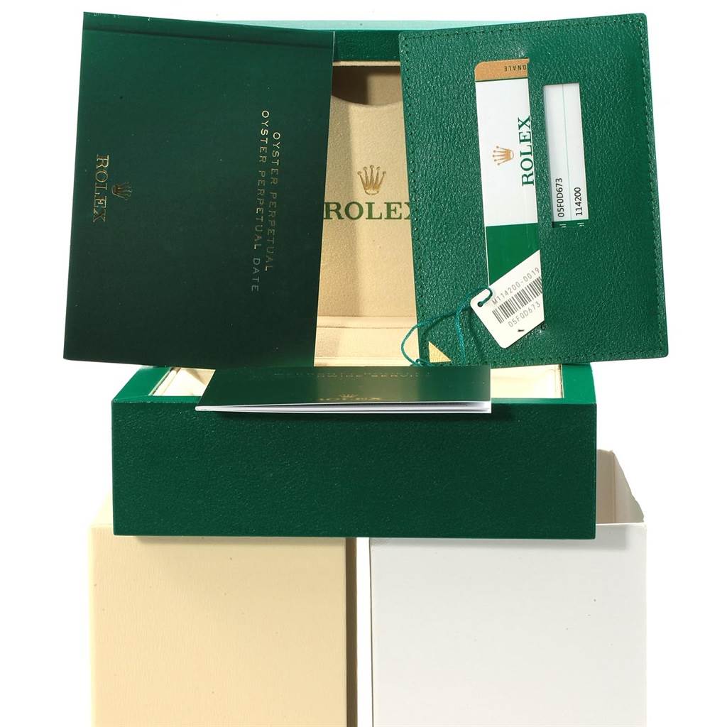 The image shows the box and documentation for a Rolex Oyster Perpetual 114200 Men's Stainless Steel Silver Dial 114200 Men's Stainless Steel Silver Dial watch, including the booklet, warranty card, and tags.
