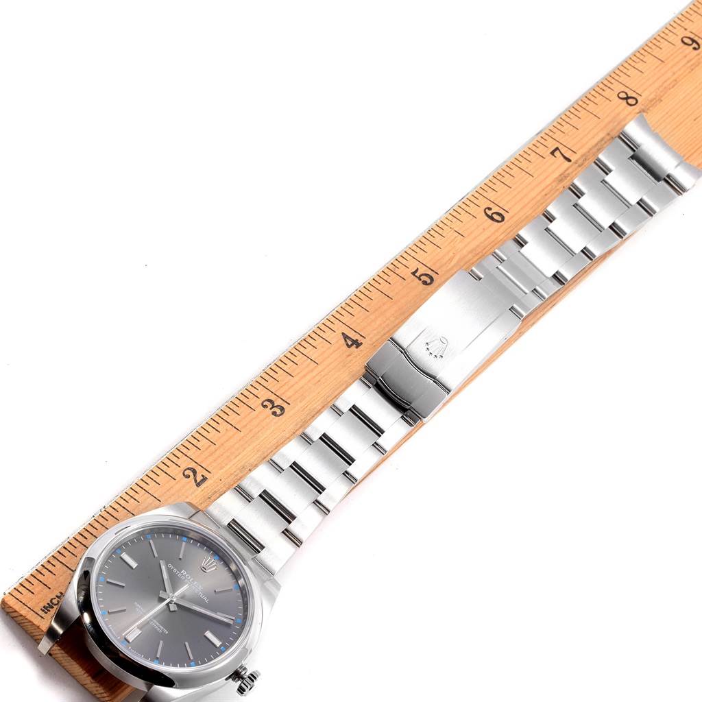The image shows a Rolex Oyster Perpetual 114300 Men's Stainless Steel Grey Dial 114300 Men's Stainless Steel Grey Dial watch laid flat against a ruler, displaying the watch face and full-length bracelet.