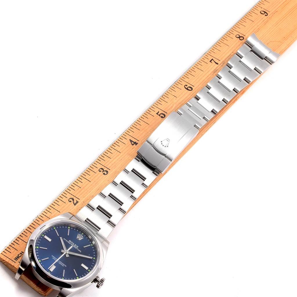 The Rolex Oyster Perpetual 114300 Men's Stainless Steel Blue Dial 114300 Men's Stainless Steel Blue Dial watch is shown laid flat, highlighting the face, bracelet, and clasp alongside a ruler for scale.