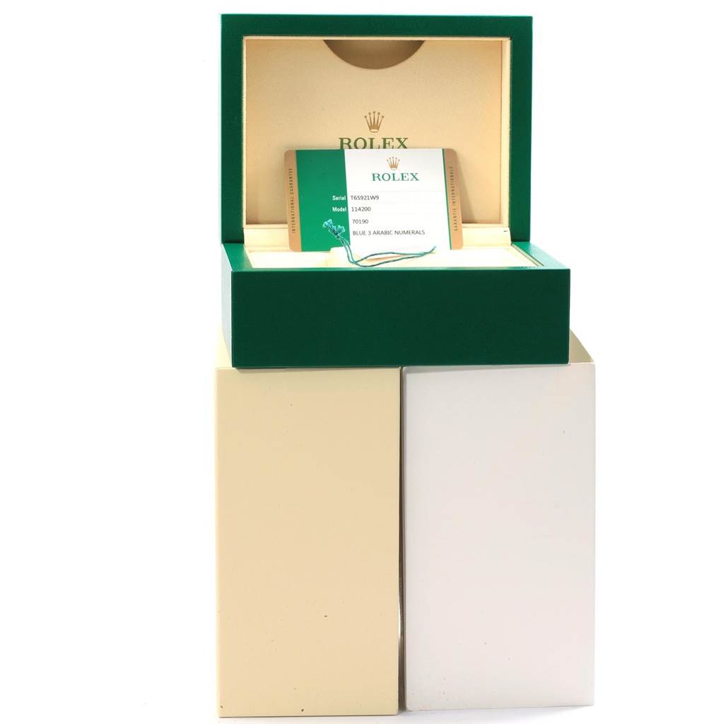 The image shows a Rolex Oyster Perpetual 114200 Men's Stainless Steel Blue Dial 114200 Men's Stainless Steel Blue Dial watch box with an open lid and documentation displayed inside.