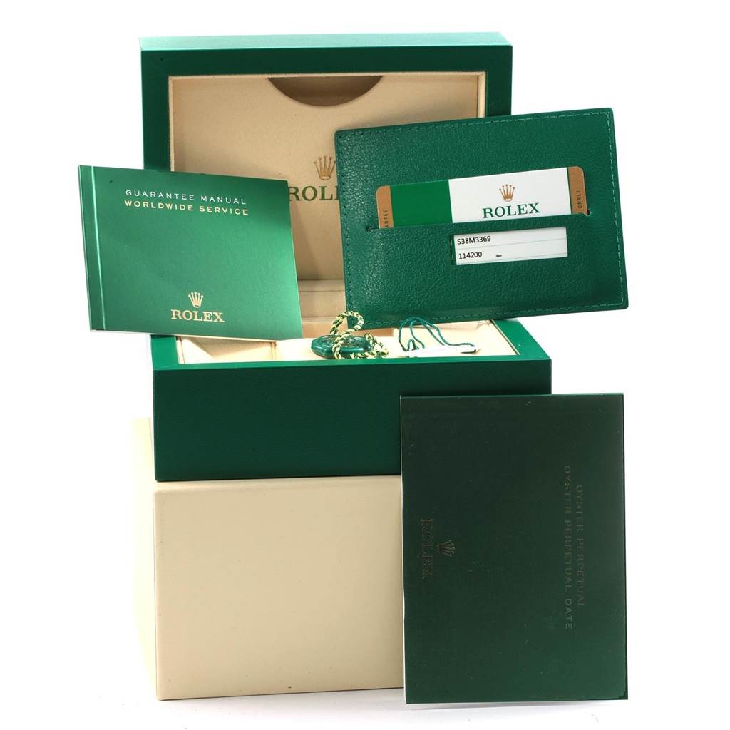 This image shows the packaging, guarantee manual, cardholder, and tags for a Rolex Oyster Perpetual 114200 Men's Stainless Steel Green Dial 114200 Men's Stainless Steel Green Dial watch.