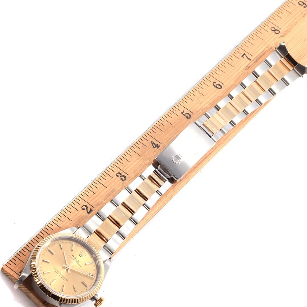 The image shows a top view of a Rolex Oyster Perpetual 14233 Men's Steel and Gold (two tone) Champagne Dial 14233 Men's Steel and Gold (two tone) Champagne Dial watch with a two-tone bracelet next to a wooden ruler.