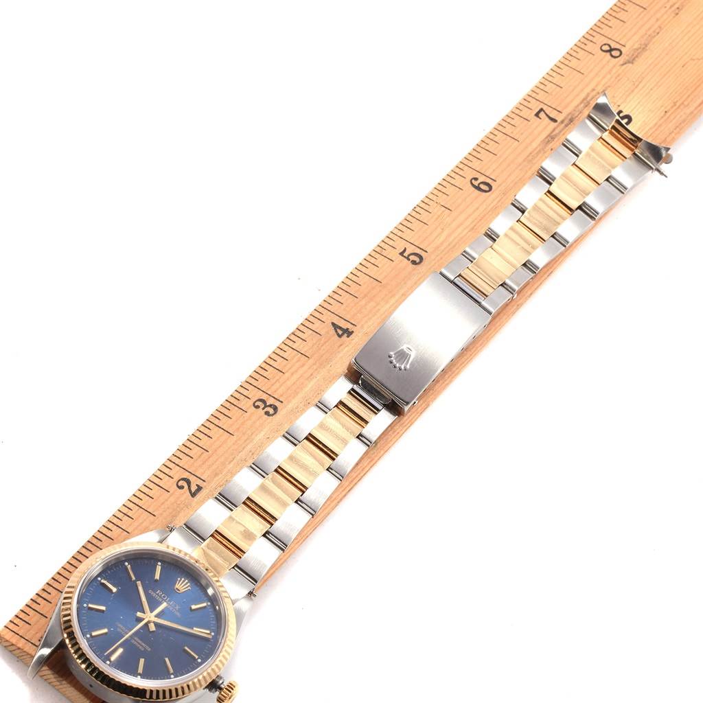 The image shows an Oyster Perpetual by Rolex from a top-down angle, displaying the blue dial and the full metal strap, next to a ruler.