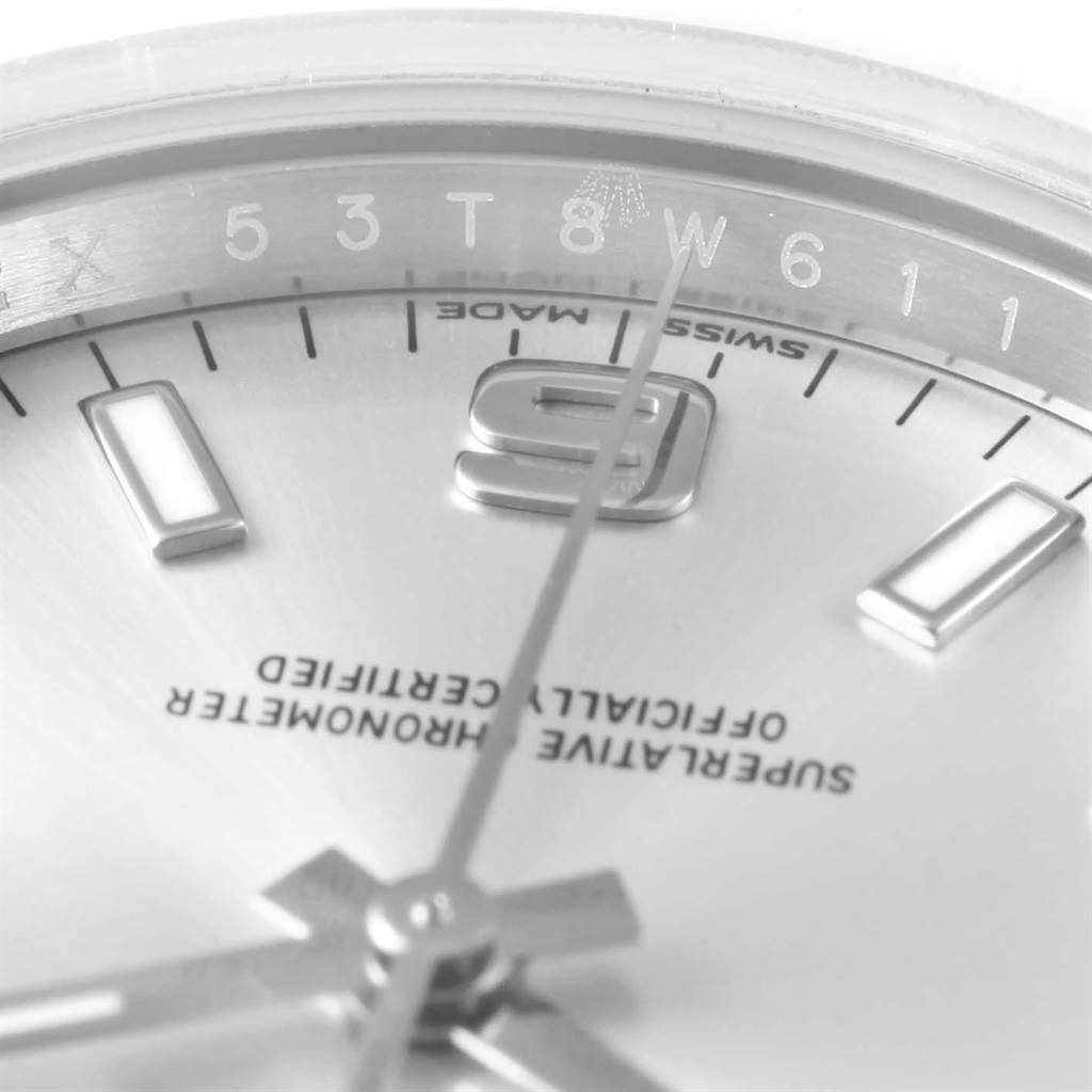 This close-up image of a Rolex Oyster Perpetual 114200 Men's Stainless Steel Silver Dial 114200 Men's Stainless Steel Silver Dial watch showcases the dial, hands, hour markers, and engravings beneath the crystal.