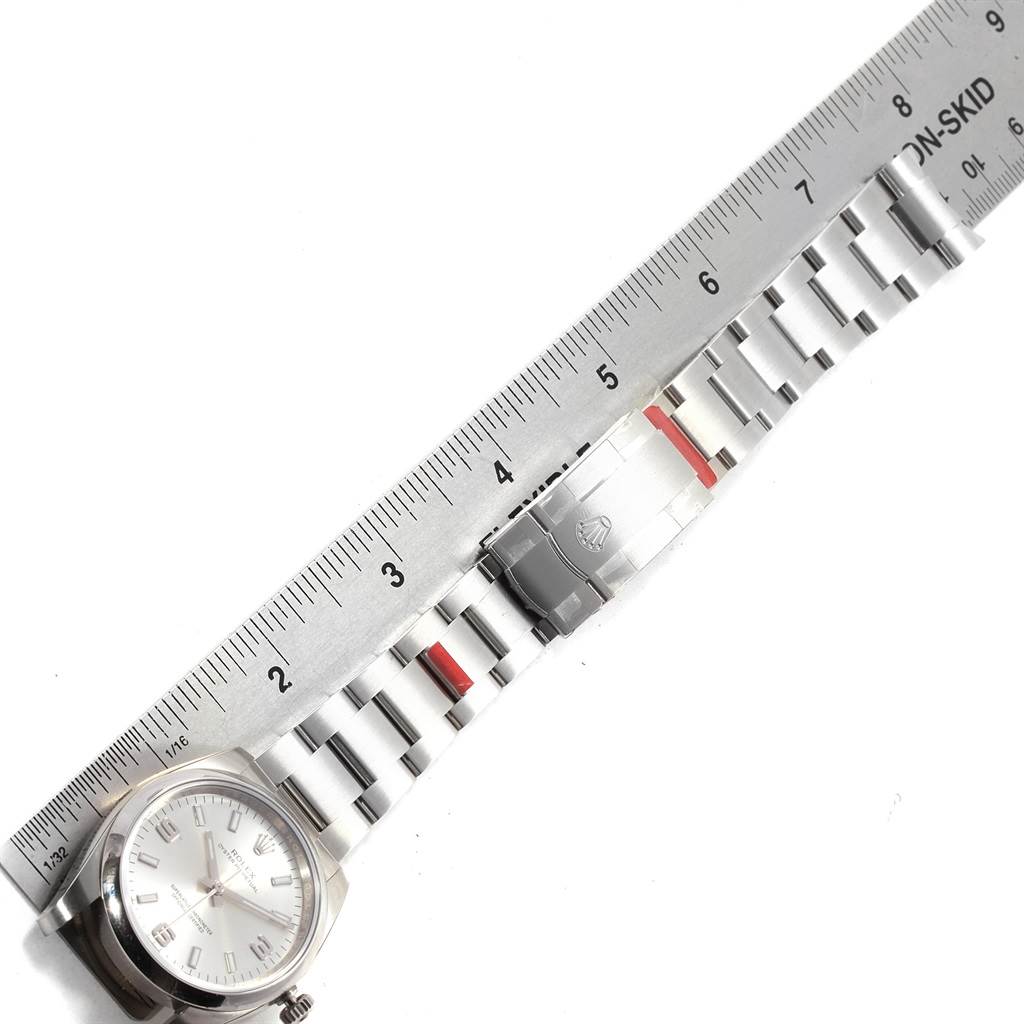 The image shows a top-down view of a Rolex Oyster Perpetual 114200 Men's Stainless Steel Silver Dial 114200 Men's Stainless Steel Silver Dial watch with a stainless steel bracelet and a ruler for size reference.