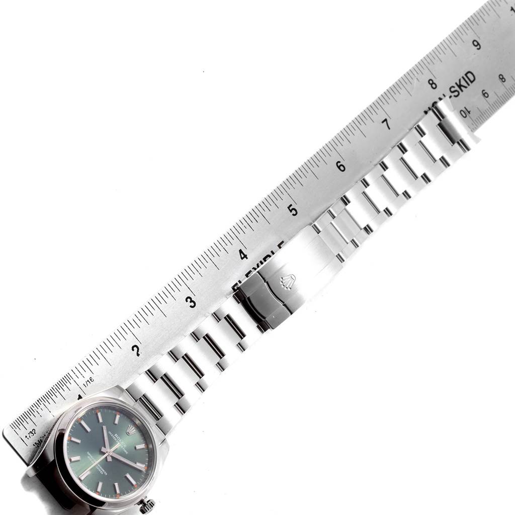 The image shows a Rolex Oyster Perpetual 114200 Stainless Steel Green Dial 114200 Stainless Steel Green Dial watch, including the face, bracelet, and clasp, laid next to a ruler for measurement.