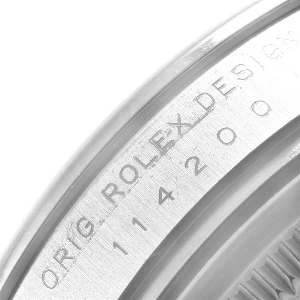 The image shows a close-up view of the engraved bezel and part of the case back of the Rolex Oyster Perpetual 114200 Men
s Stainless Steel Green Dial 114200 Men
s Stainless Steel Green Dial watch.