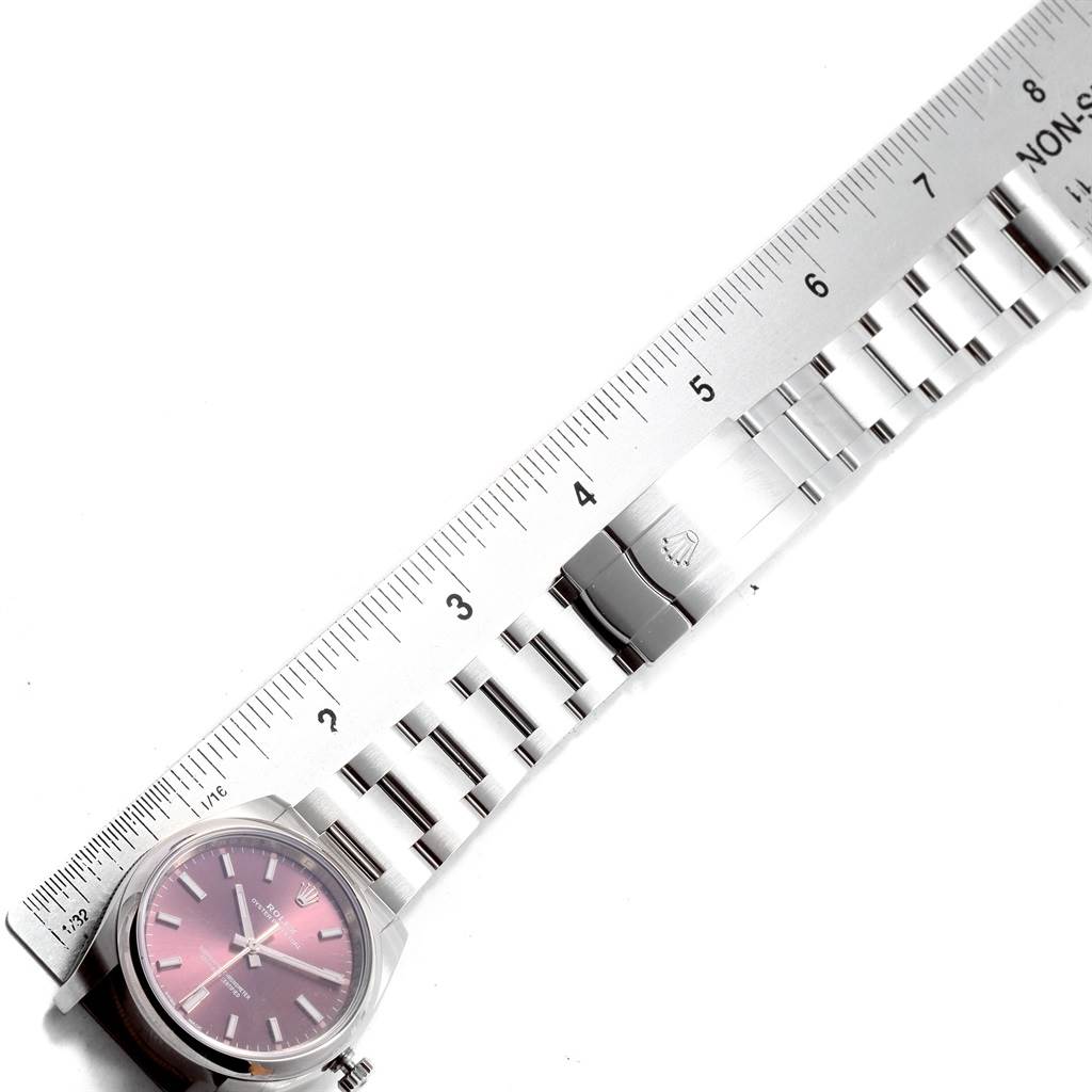 This image shows a top-down view of a Rolex Oyster Perpetual 114200 Stainless Steel Burgundy Dial 114200 Stainless Steel Burgundy Dial watch, including its face, partially extended metal bracelet, and a ruler for scale.