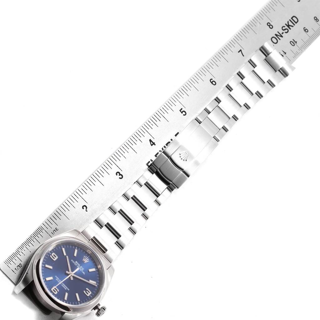 The image shows a Rolex Oyster Perpetual 116000 Men's Stainless Steel Blue Dial 116000 Men's Stainless Steel Blue Dial watch with a blue dial and its metal bracelet measured against a ruler.