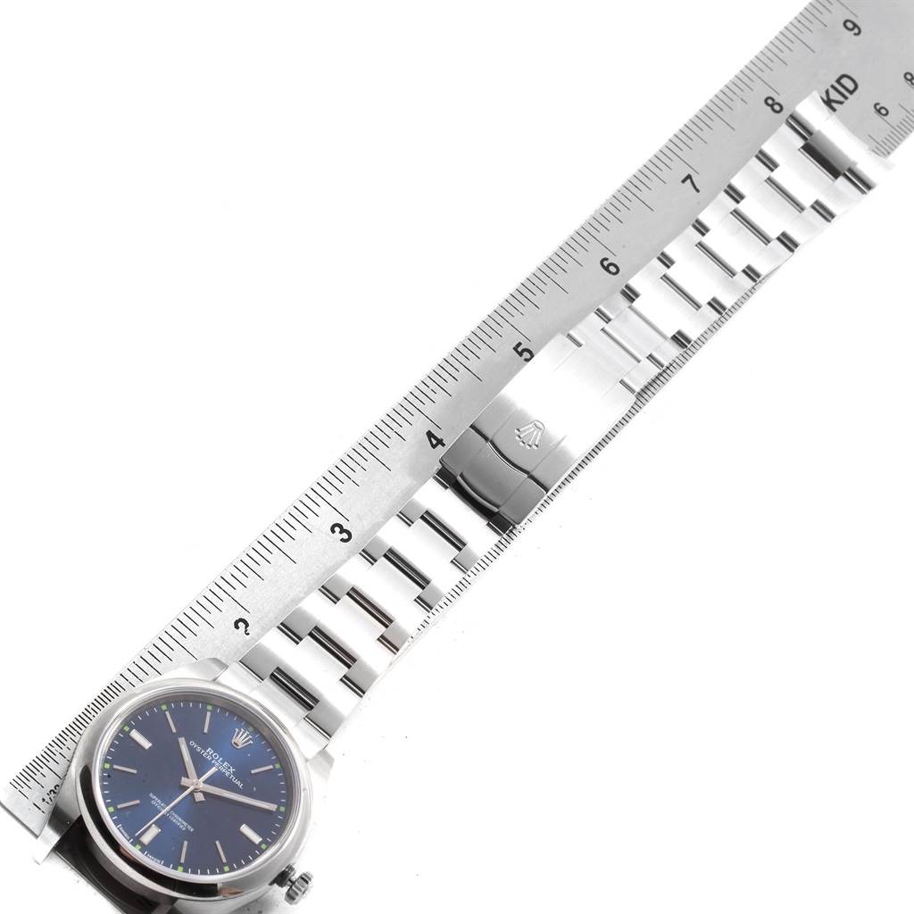 This image displays the Rolex Oyster Perpetual 114300 Men
s Stainless Steel Blue Dial 114300 Men
s Stainless Steel Blue Dial watch face and metal bracelet alongside a measuring ruler.