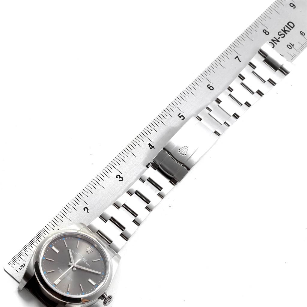 The image shows the face and bracelet of a Rolex Oyster Perpetual 114300 Men
s Stainless Steel Grey Dial 114300 Men
s Stainless Steel Grey Dial watch alongside a ruler for measurement.