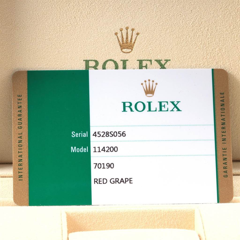 The image shows a warranty card for a Rolex Oyster Perpetual 114200 Men
s Stainless Steel Burgundy Dial 114200 Men
s Stainless Steel Burgundy Dial model 114200, placed in a beige Rolex box.