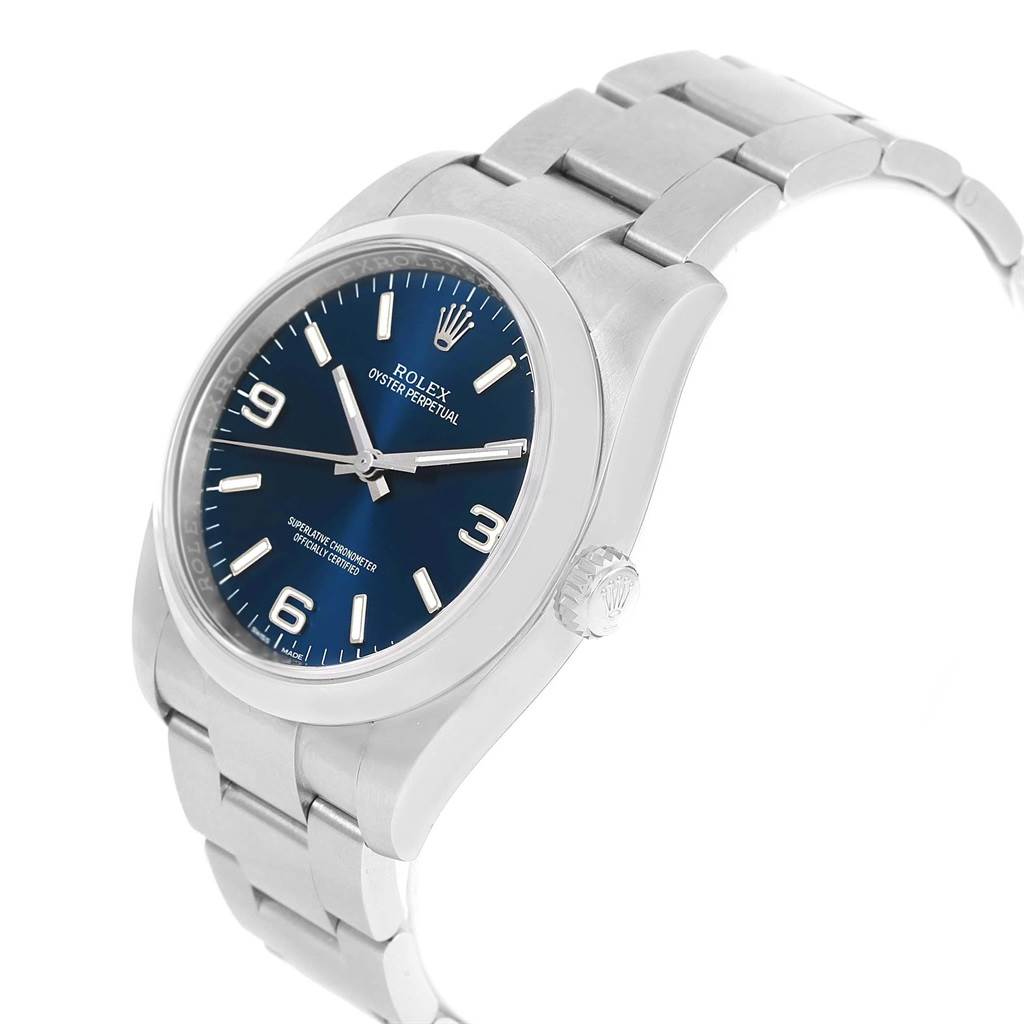 The image shows an angled view of a Rolex Oyster Perpetual 116000 Men
s Stainless Steel Blue Dial 116000 Men
s Stainless Steel Blue Dial watch, highlighting the face, crown, and part of the bracelet.