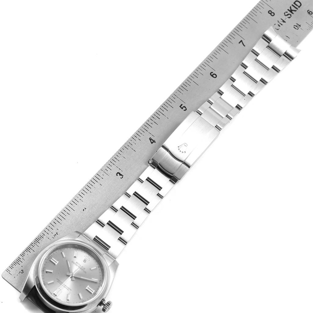 The image shows a top-down view of a Rolex Oyster Perpetual 116000 Men
s Stainless Steel Grey Dial 116000 Men
s Stainless Steel Grey Dial watch, including its bracelet and clasp, alongside a ruler for scale.