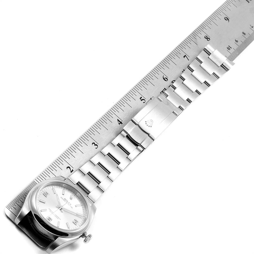 The image shows a top view of a Rolex Oyster Perpetual 116000 Men
s Stainless Steel Silver Dial 116000 Men
s Stainless Steel Silver Dial watch laid beside a ruler, highlighting its bracelet and clasp.