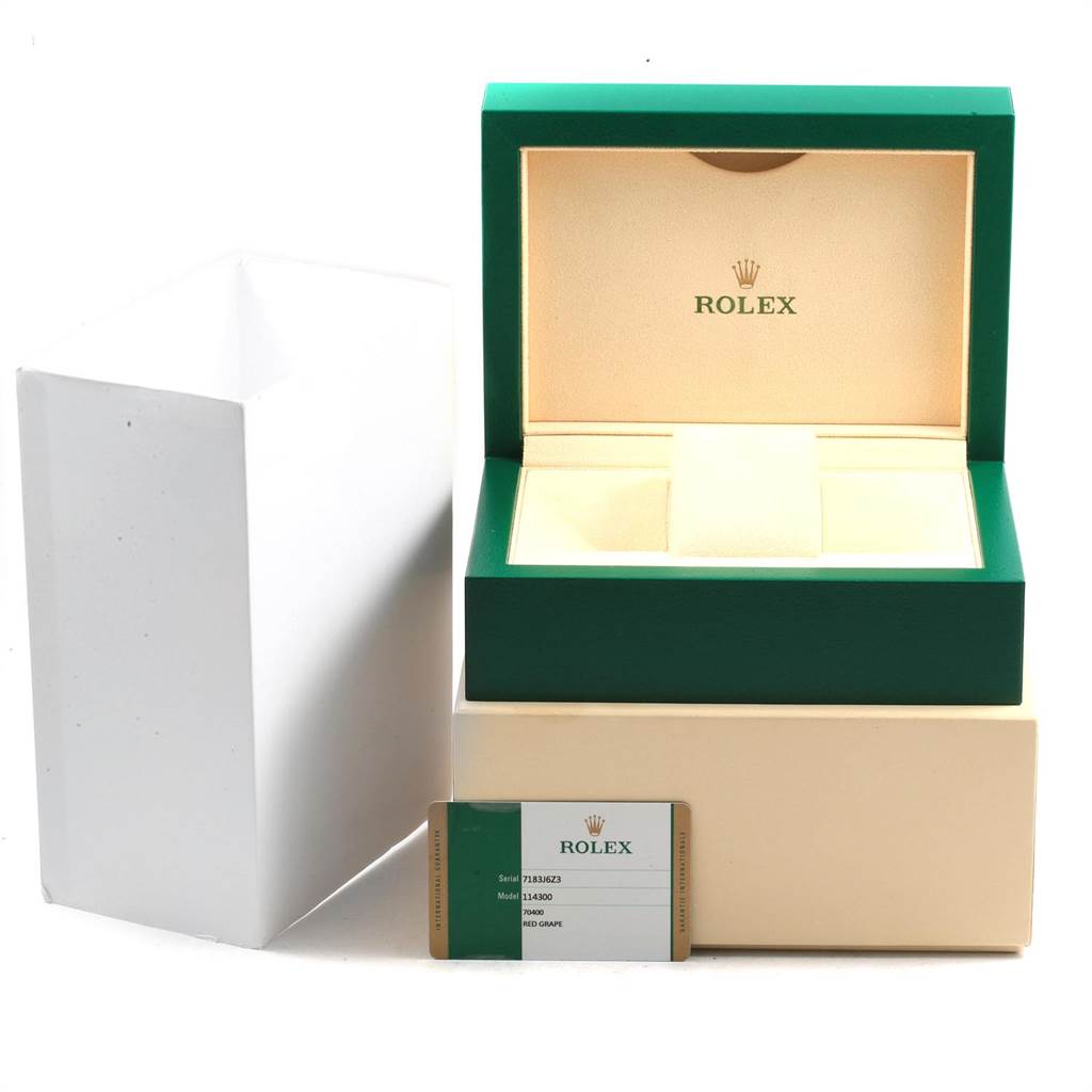 The image shows the packaging and warranty card for a Rolex Oyster Perpetual 114300 Men's Stainless Steel Burgundy Dial 114300 Men's Stainless Steel Burgundy Dial watch from a front angle.