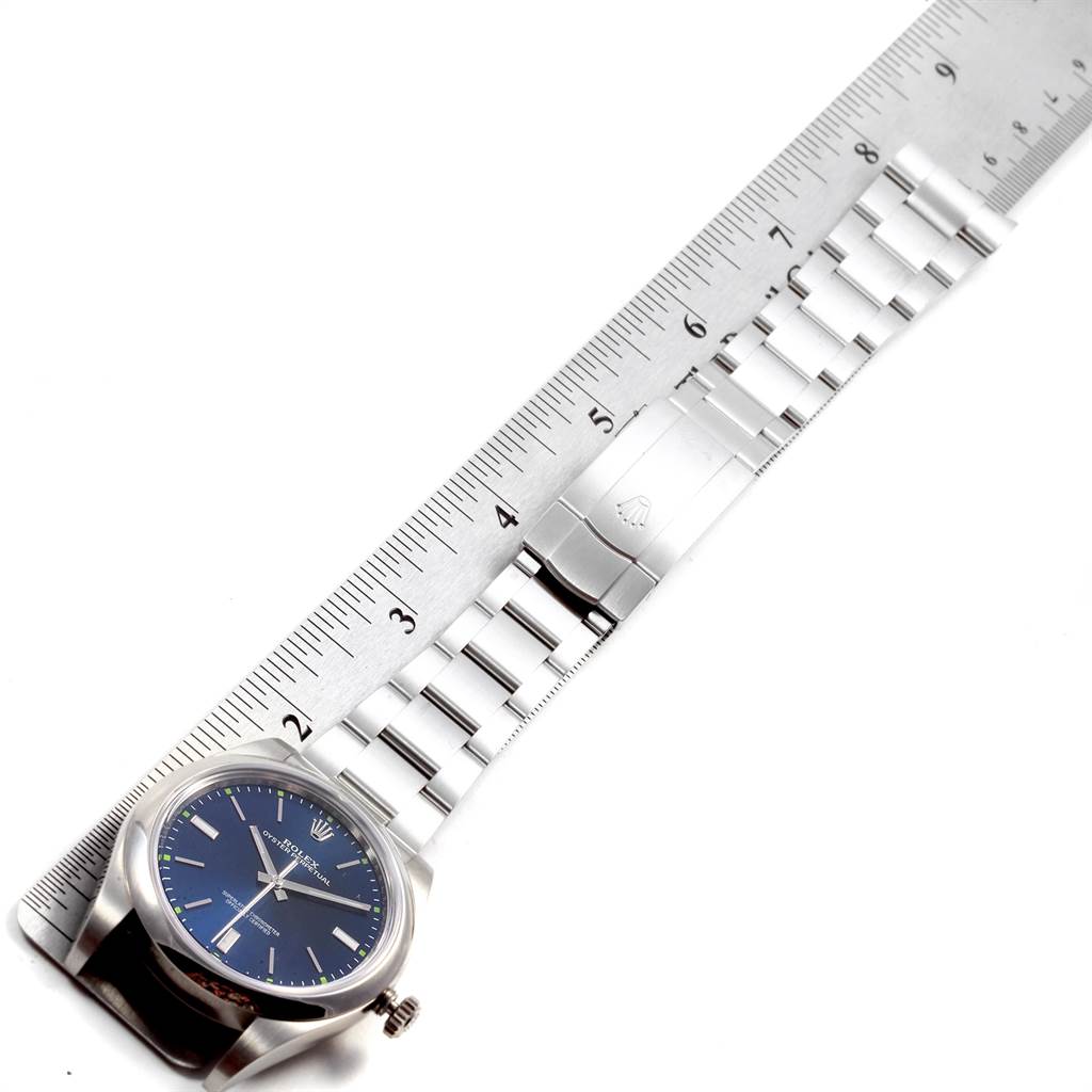 The Rolex Oyster Perpetual 114300 Men
s Stainless Steel Blue Dial 114300 Men
s Stainless Steel Blue Dial watch is shown laid flat with its entire band, alongside a ruler for measurement.