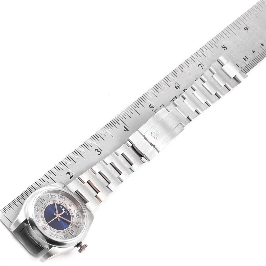 The image shows an aerial view of a Rolex Oyster Perpetual 116000 Men
s Stainless Steel Silver Dial 116000 Men
s Stainless Steel Silver Dial watch and its metal bracelet, placed alongside a ruler for measurement.