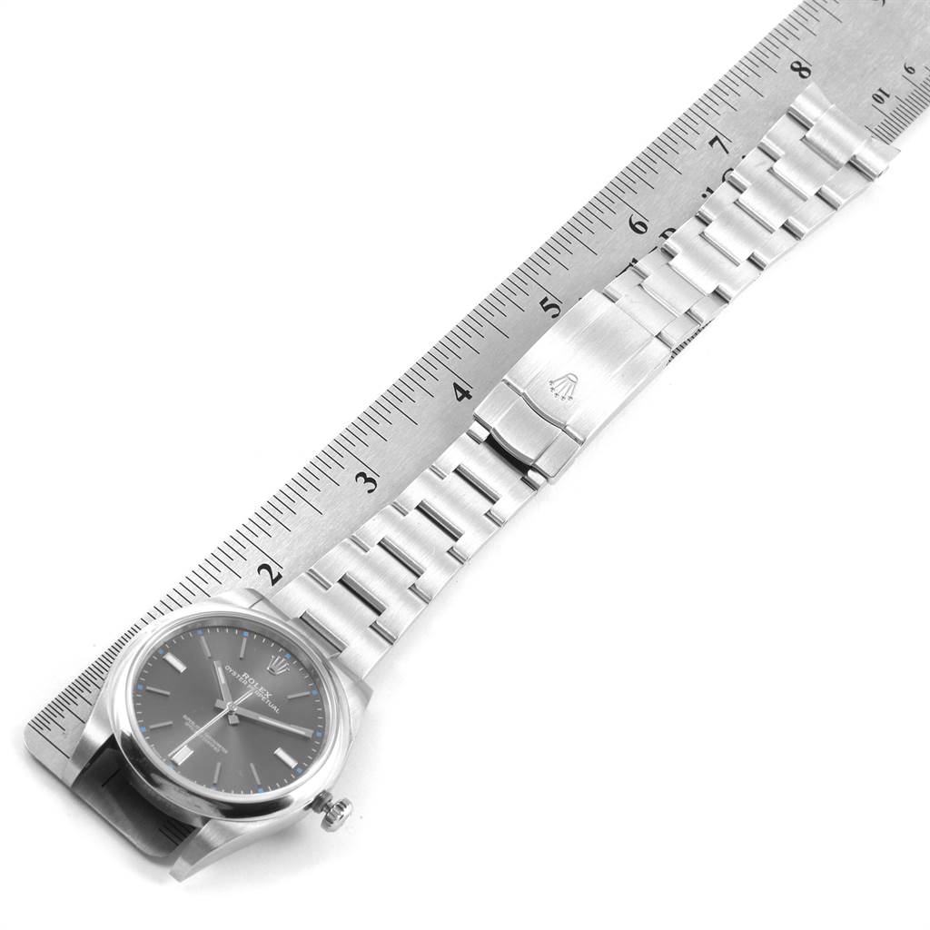 The image shows a top-down view of a Rolex Oyster Perpetual 114300 Men
s Stainless Steel Grey Dial 114300 Men
s Stainless Steel Grey Dial watch with its full metal band alongside a ruler.